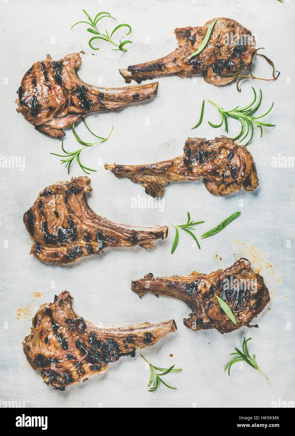 Grilled lamb ribs with fresh rosemary over metal baking tray background, top view, vertical composition. Meat barbecue and slow food concept Stock Photo