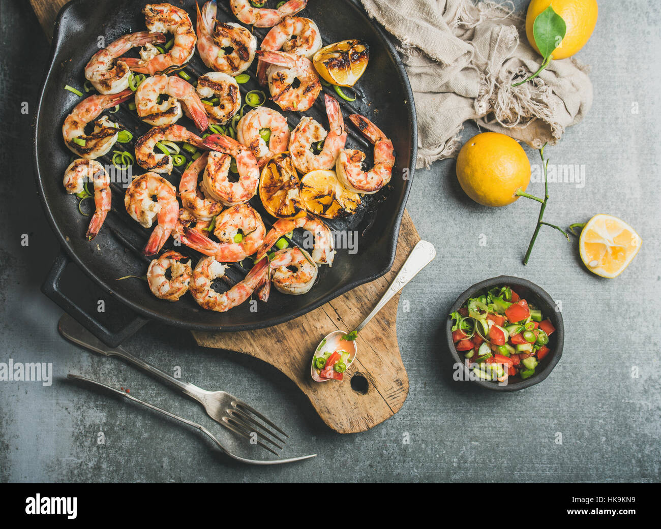 Seafood dinner. Grilled tiger prawns in cast iron grilling pan with lemon, leek, chili pepper and mint salsa sauce over grey concrete background, top Stock Photo