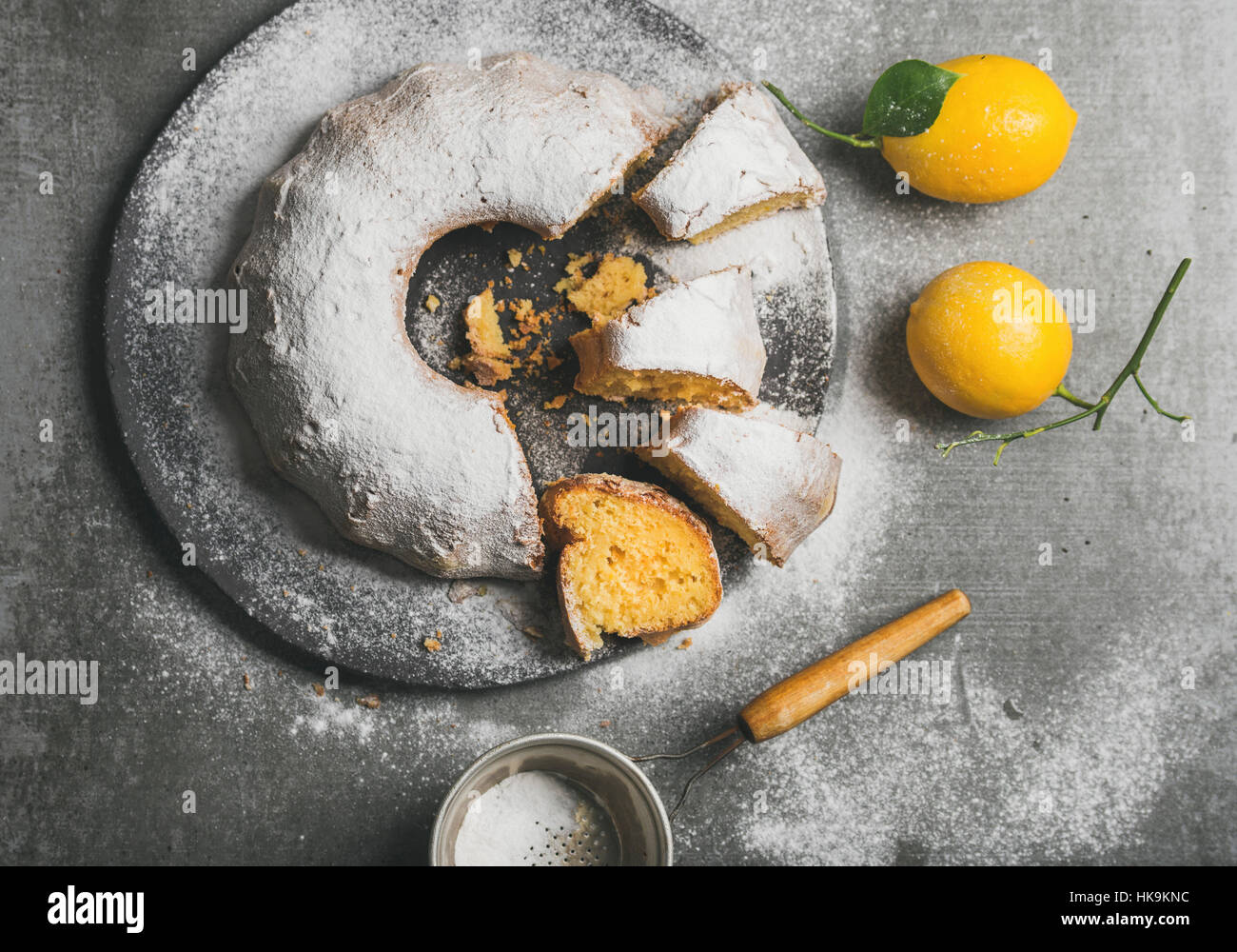 Homemade gluten-free lemon bundt cake with sugar powder served with freshly picked lemons over grey concrete background, top view Stock Photo