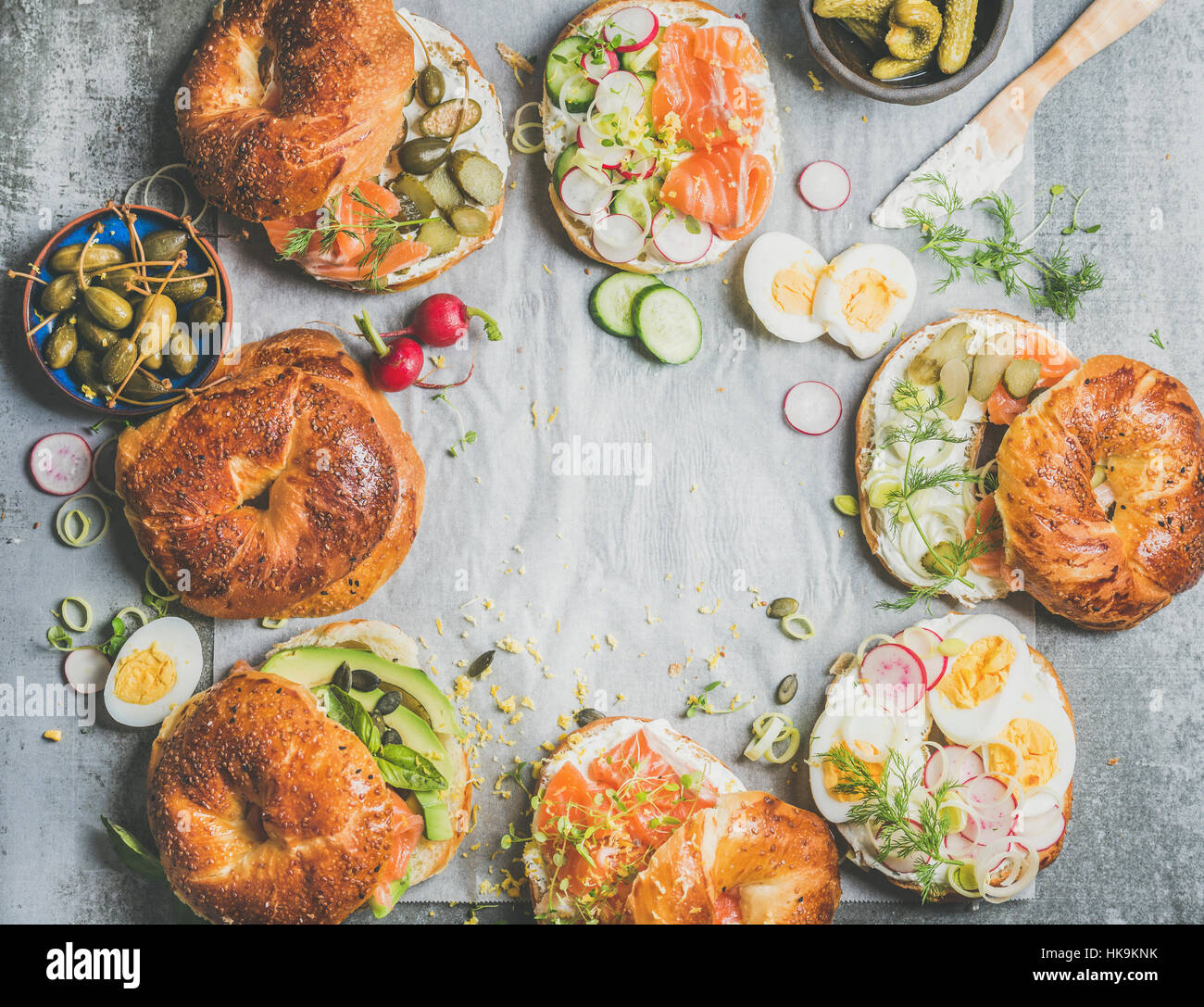 Variety of bagels with salmon, eggs, radish, avocado, cucumber, greens and cream cheese for breakfast, healthy lunch or party over grey concrete backg Stock Photo