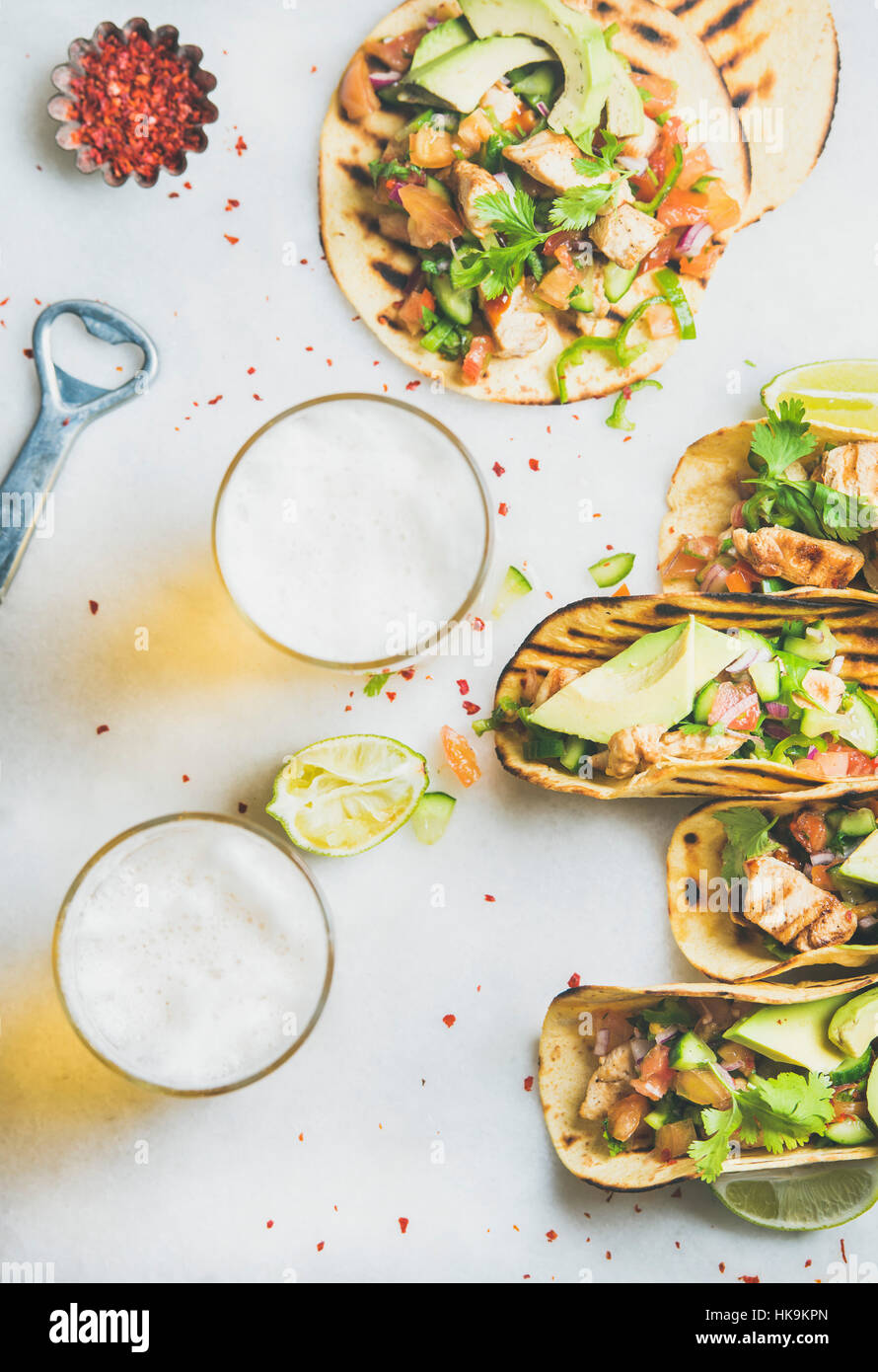 Healthy corn tortillas with grilled chicken, avocado, fresh salsa, limes, beer in glasses over light grey marble background, top view. Healthy food, g Stock Photo
