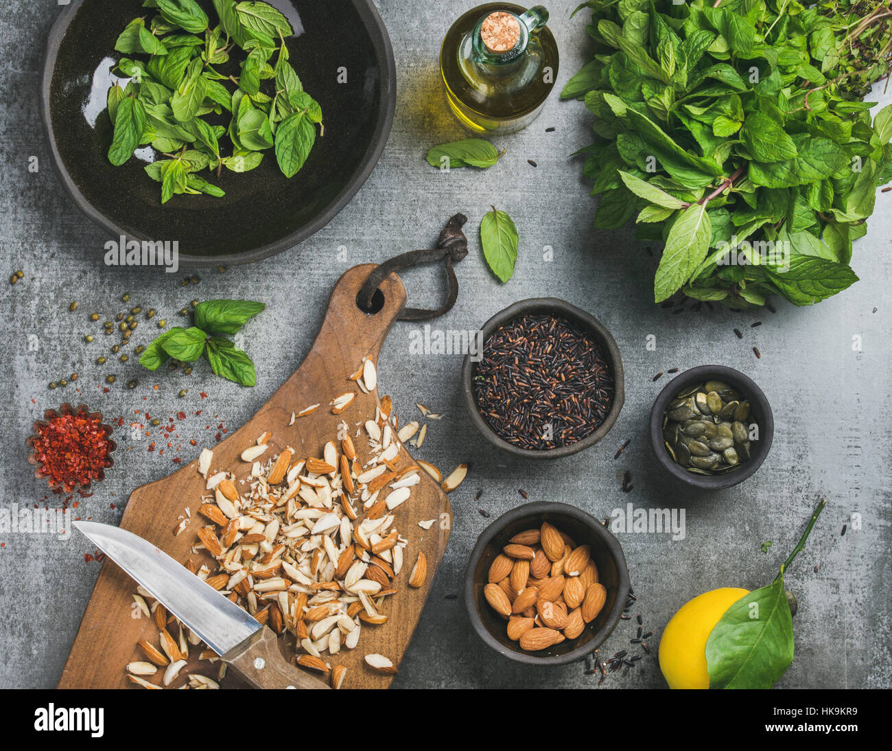 Healthy, vegetarian, vegan or clean eating cooking ingredients. Chopped almonds, fresh mint, oil, black rice, pumpkin seeds spices, lemon over grey co Stock Photo