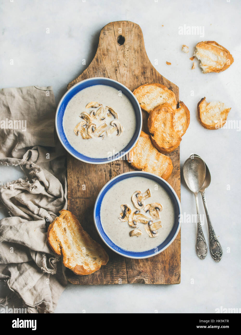 Creamy mushroom soup in bowls with toasted bread slices on rustic serving board over grey marble background, top view, selective focus Stock Photo