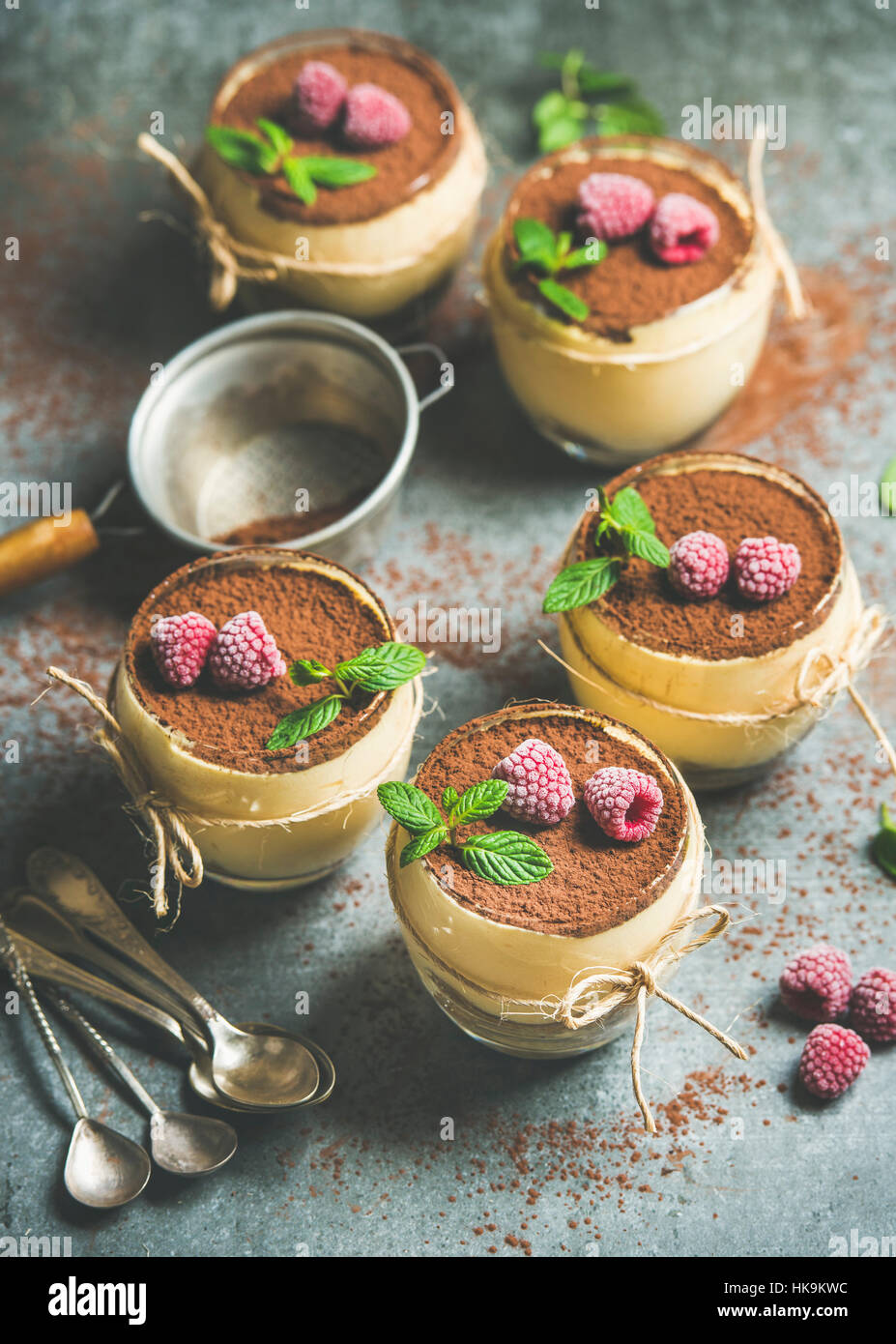 Homemade Italian dessert Tiramisu served in individual glasses with frozen raspberries, fresh mint leaves and cocoa powder over grey concrete backgrou Stock Photo