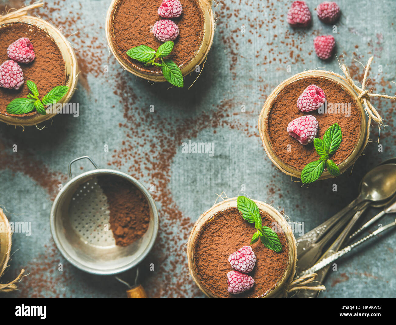 Homemade Italian dessert Tiramisu served in individual glasses with mint leaves and cocoa powder over grey concrete background, top view, selective fo Stock Photo