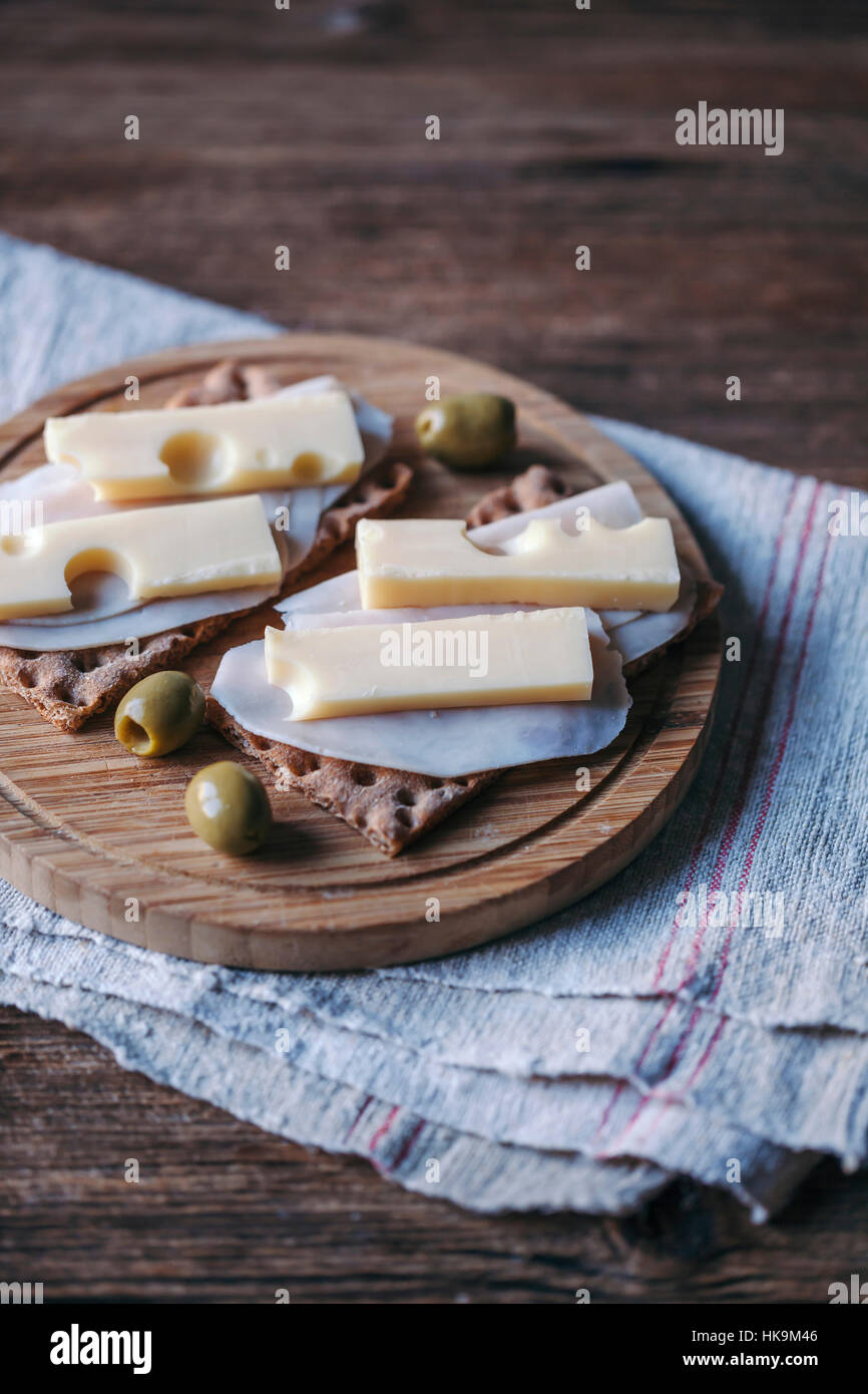 Ham and cheese crisp bread sandwiches and olives served on a wooden cutting board Stock Photo