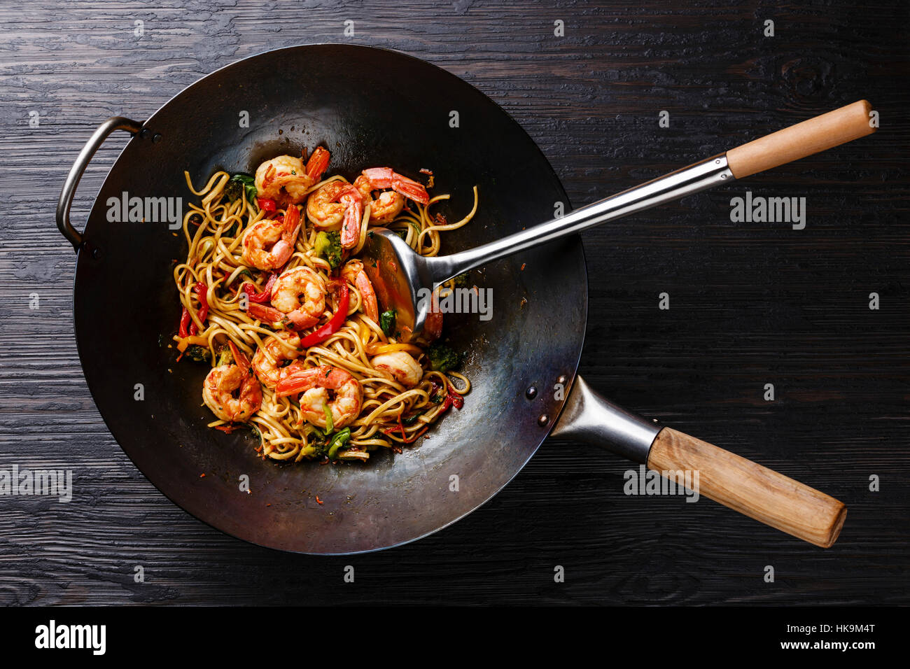 Udon stirfry noodles with shrimp and vegetables in wok pan on black