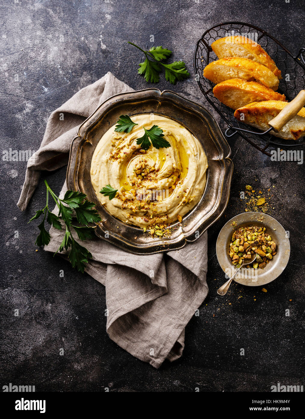 Homemade hummus with pistachios and bread toasts in metal plate on black stone background Stock Photo