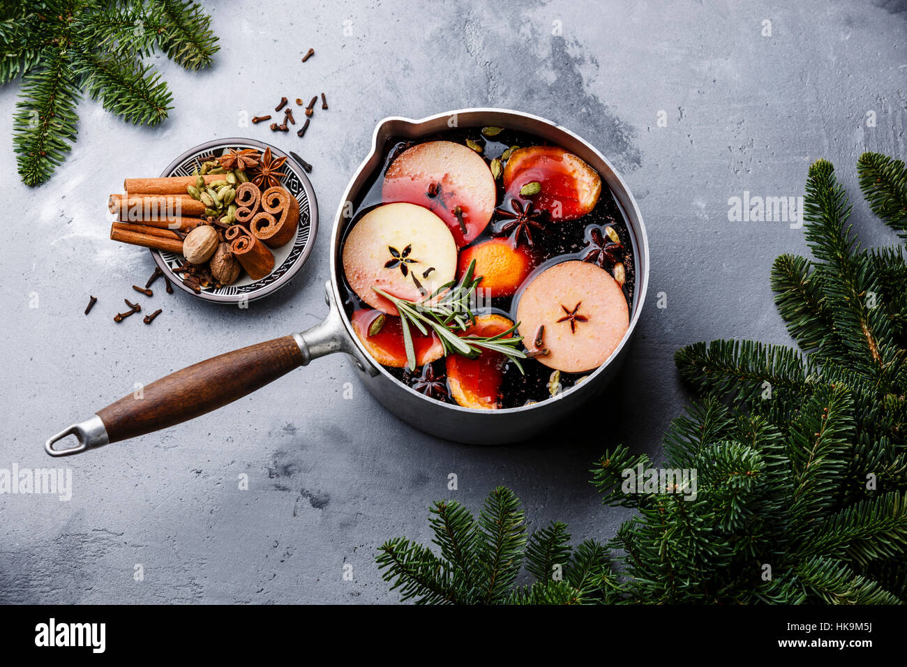 Mulled wine hot drink with citrus, apple and spices in aluminum casserole and Fir branch on concrete background Stock Photo