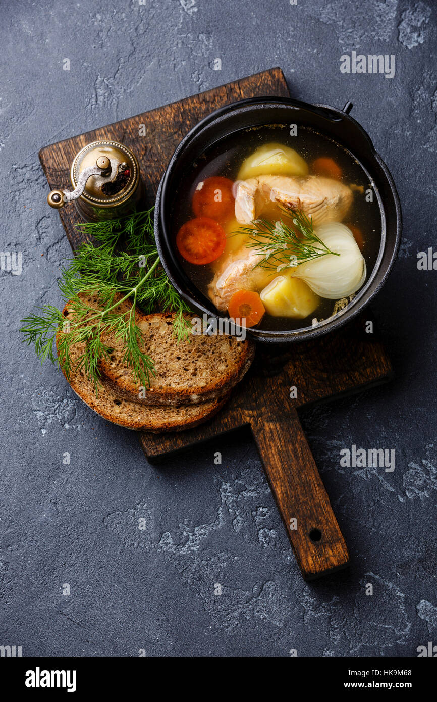 Fish soup with salmon, potato and carrot in black iron pot on dark stone background Stock Photo