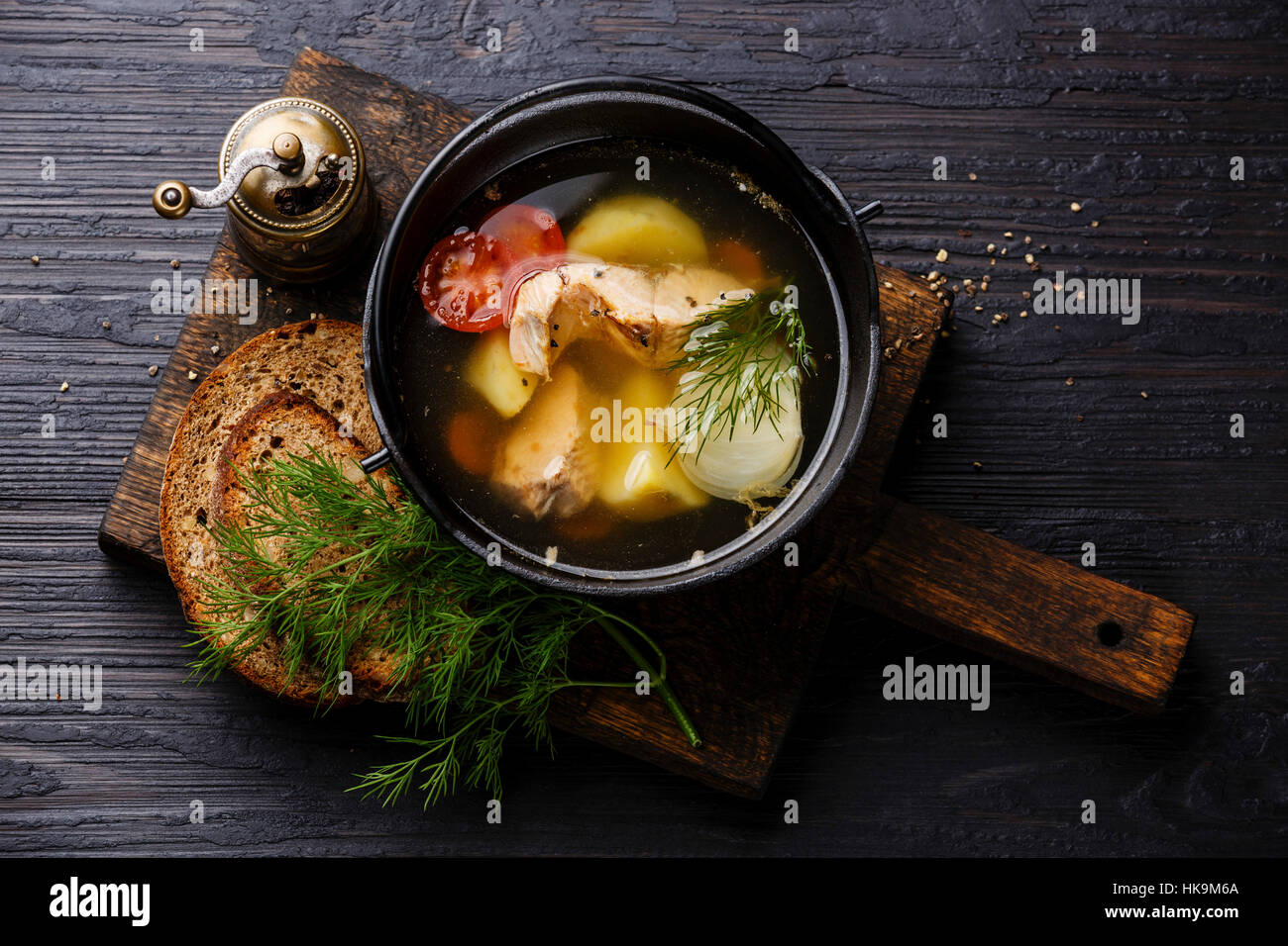 Fish soup with salmon, potato and carrot in black iron pot on black burned wooden background Stock Photo