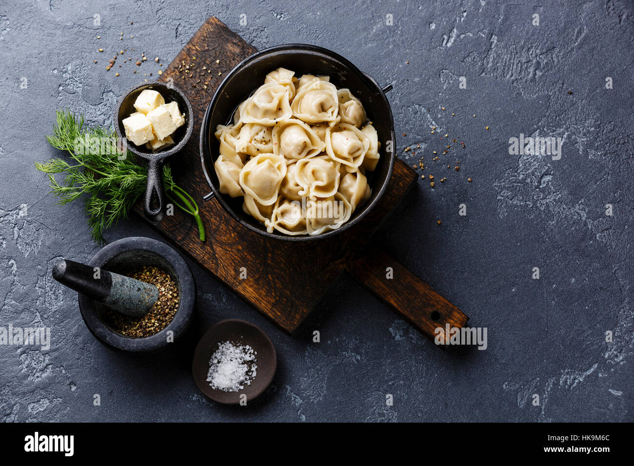 Russian pelmeni meat Dumplings with butter in black iron pot on dark stone background copy space Stock Photo