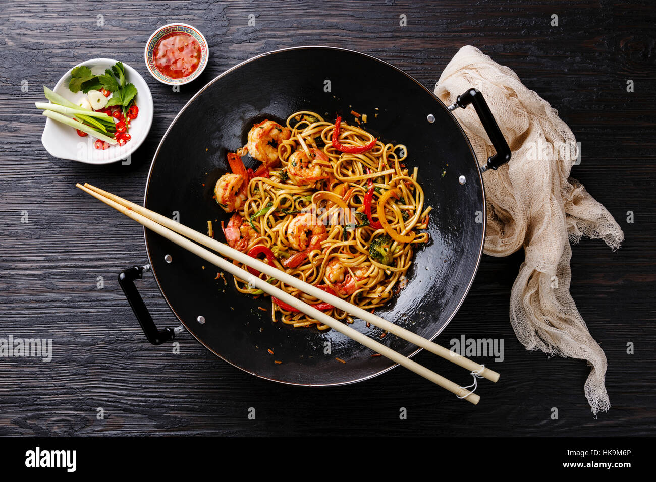 Udon stirfry noodles with shrimp and vegetables in wok pan on black