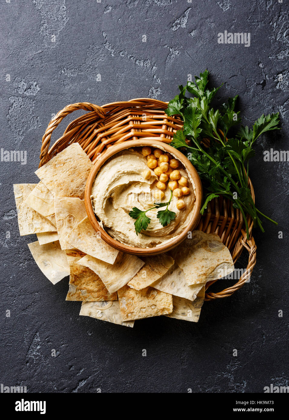 Homemade hummus with pita chips and parsley on black stone background
