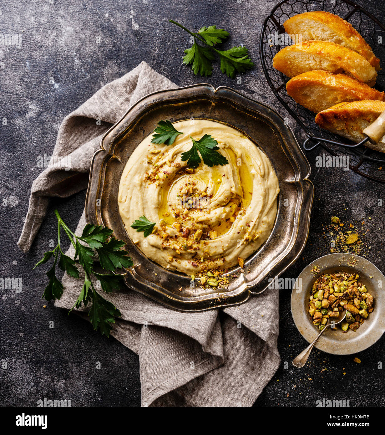 Homemade hummus with pistachios and bread toasts in metal plate on black stone background close up Stock Photo