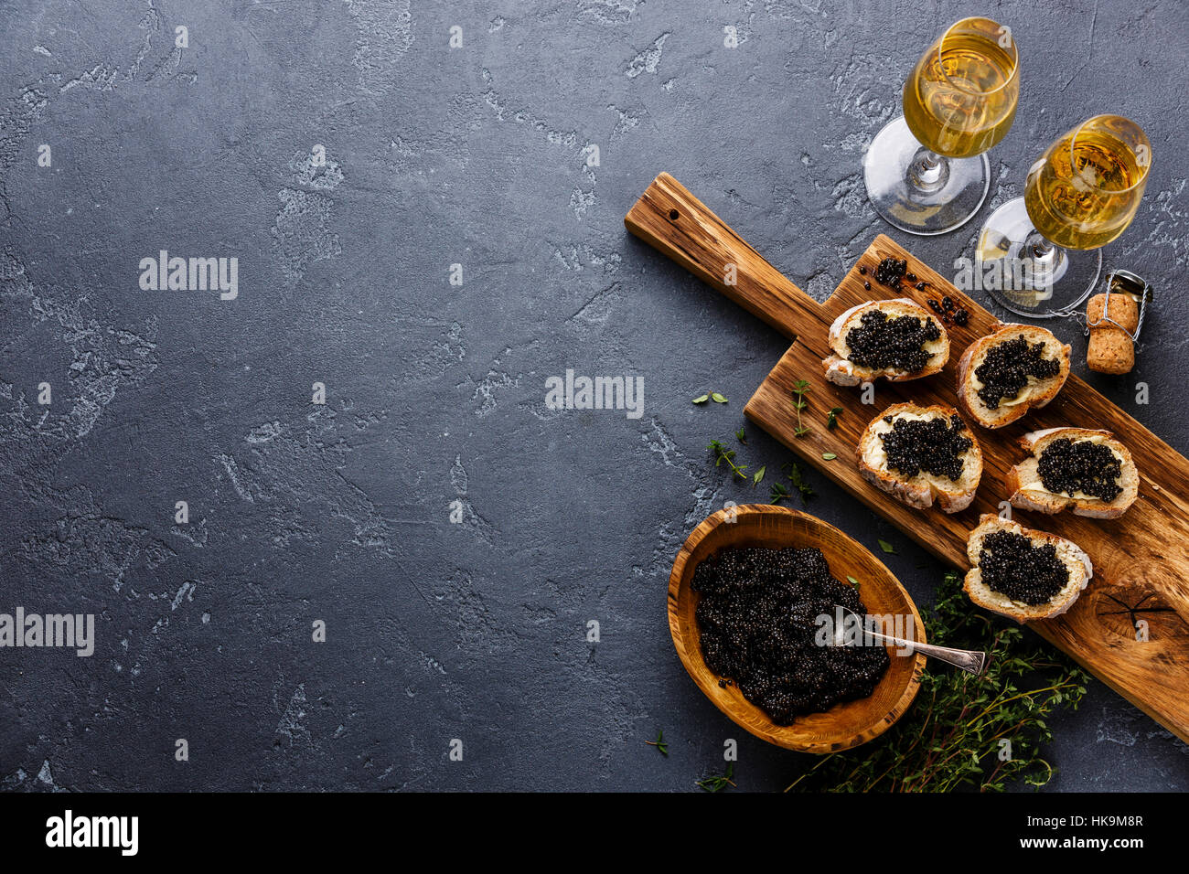 Sturgeon black caviar in wooden bowl, sandwiches and champagne on dark stone background copy space Stock Photo