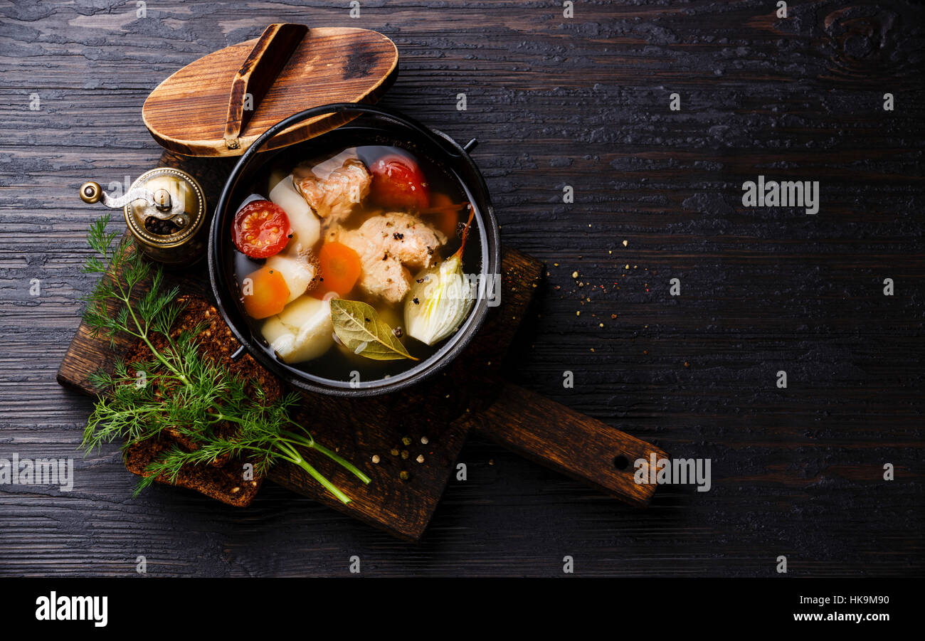 Fish soup with salmon, potato and carrot in black iron pot on black burned wooden background copy space Stock Photo