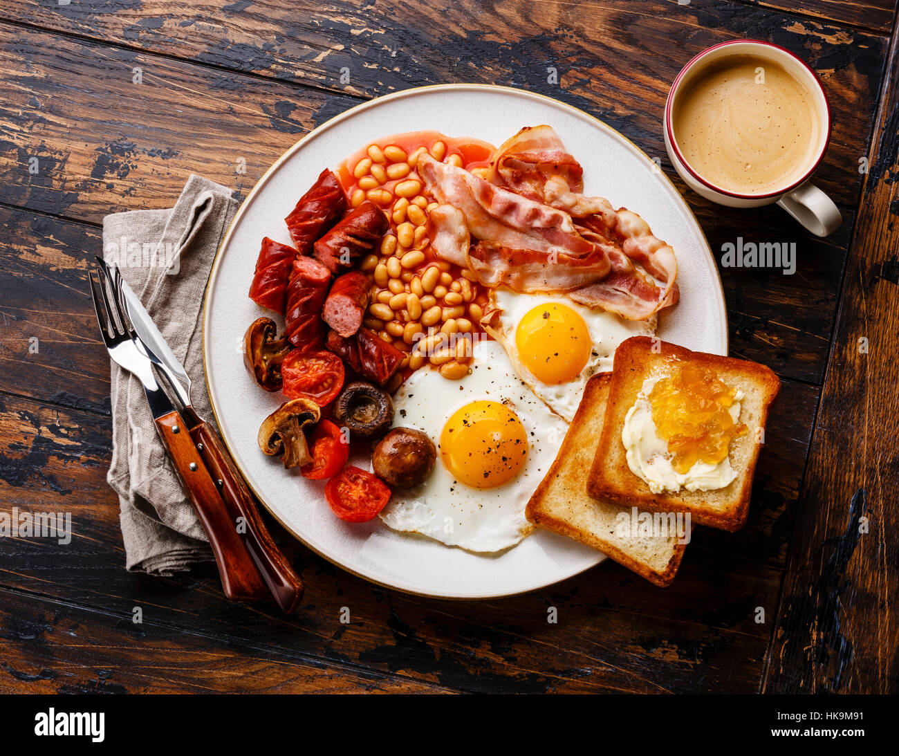 English breakfast with fried eggs, sausages, bacon, beans, toasts and coffee on wooden background Stock Photo