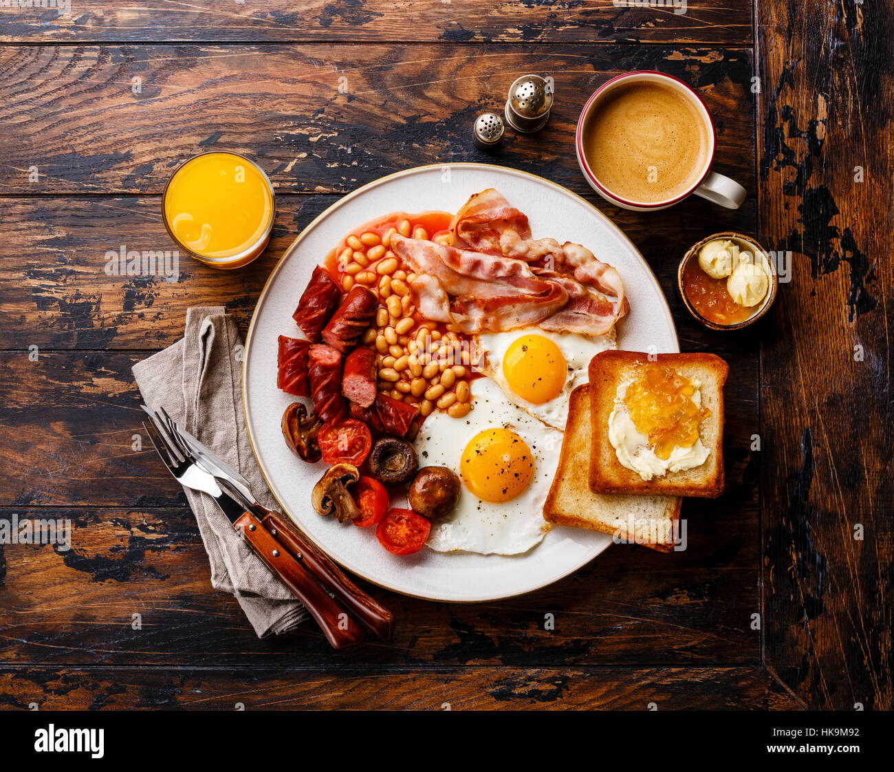 Full English breakfast with fried eggs, sausages, bacon, beans, toasts and coffee on wooden background Stock Photo