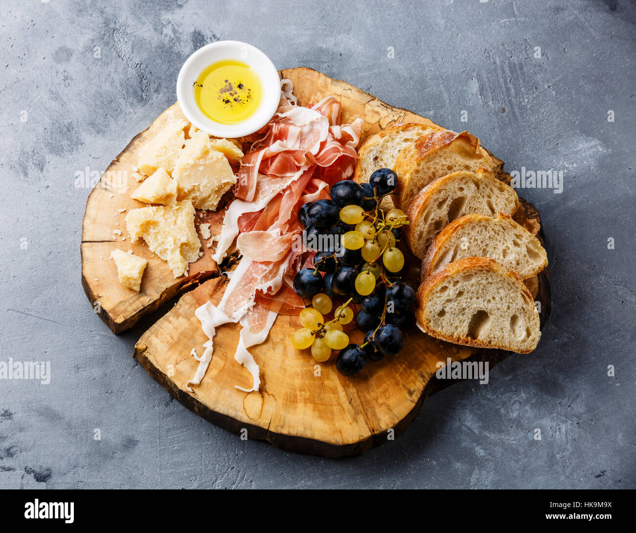 Appetizer plate with prosciutto, parmesan cheese and bread on wooden board on gray concrete background Stock Photo
