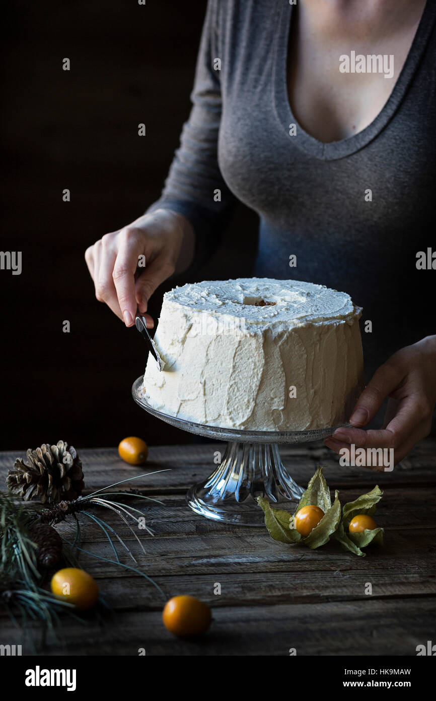 Woman is frosting a chiffon cake on wooden table Stock Photo