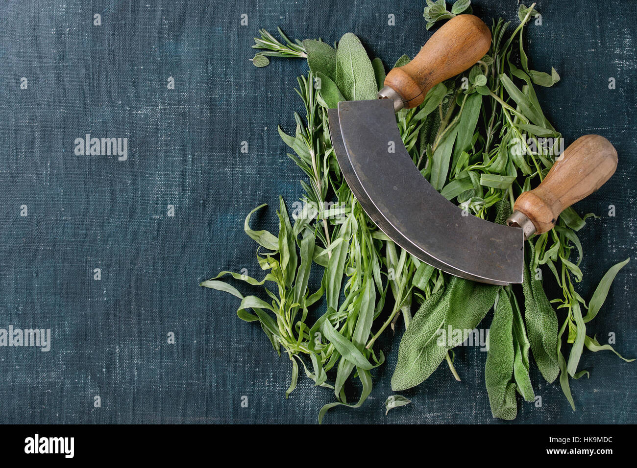 Bundle of fresh Italian herbs rosemary, oregano and sage with vintage herb cutter over dark blue shabby background. Top view with copy space Stock Photo