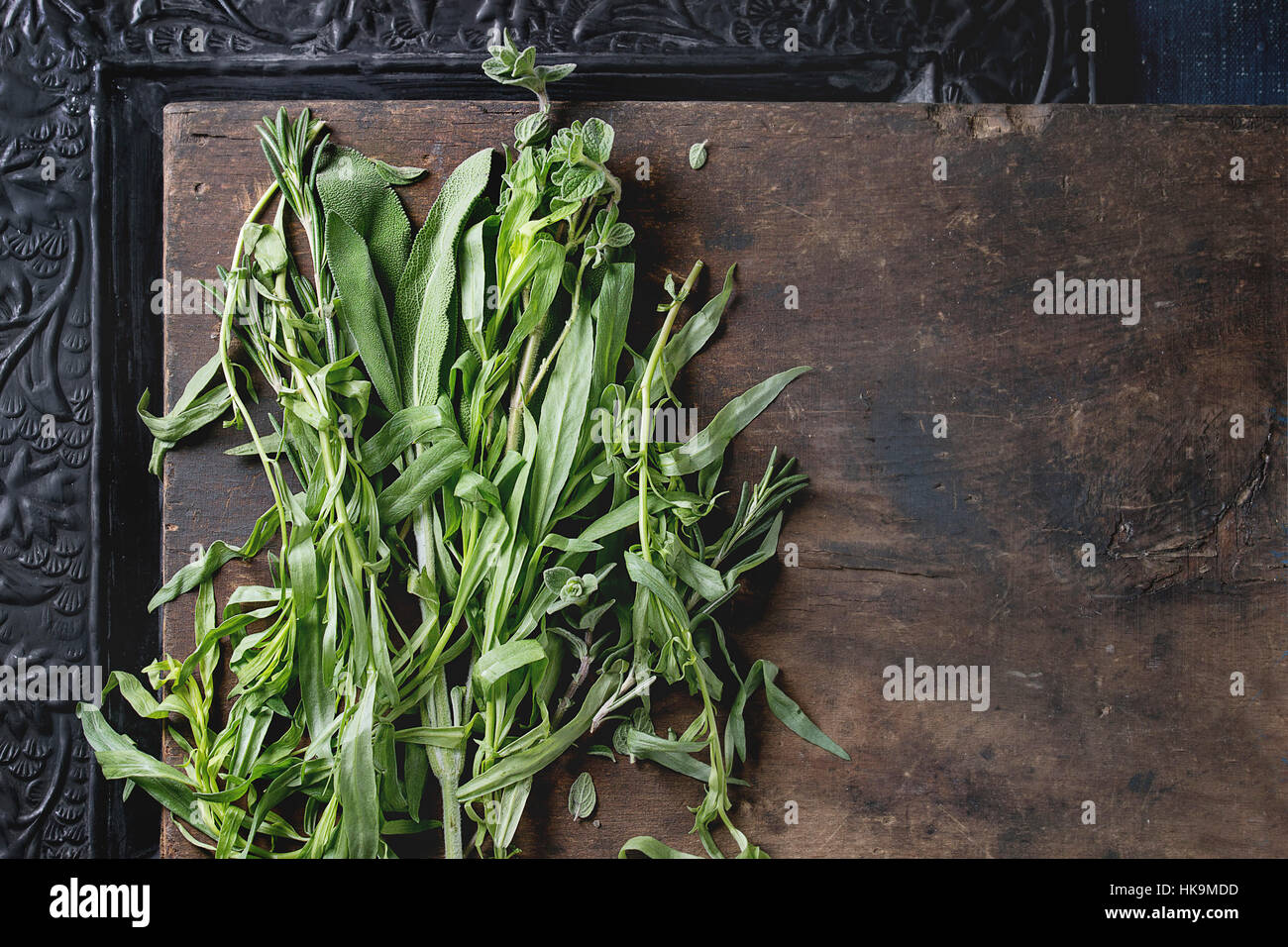 Bundle of fresh Italian herbs rosemary, oregano and sage over old dark wooden and black ornate background. Top view with copy space Stock Photo