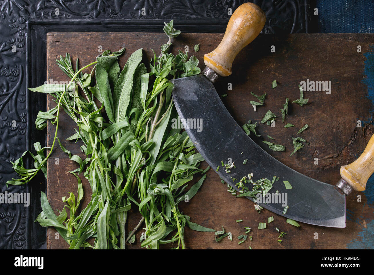 Bundle of fresh Italian herbs rosemary, oregano and sage with vintage herb cutter over old dark wooden and black ornate background. Top view Stock Photo