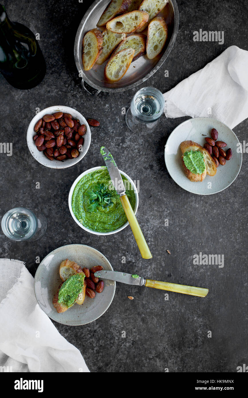 Arugula Chive Basil Pesto served in a ceramic bowl with crostini, almonds and wine. Stock Photo