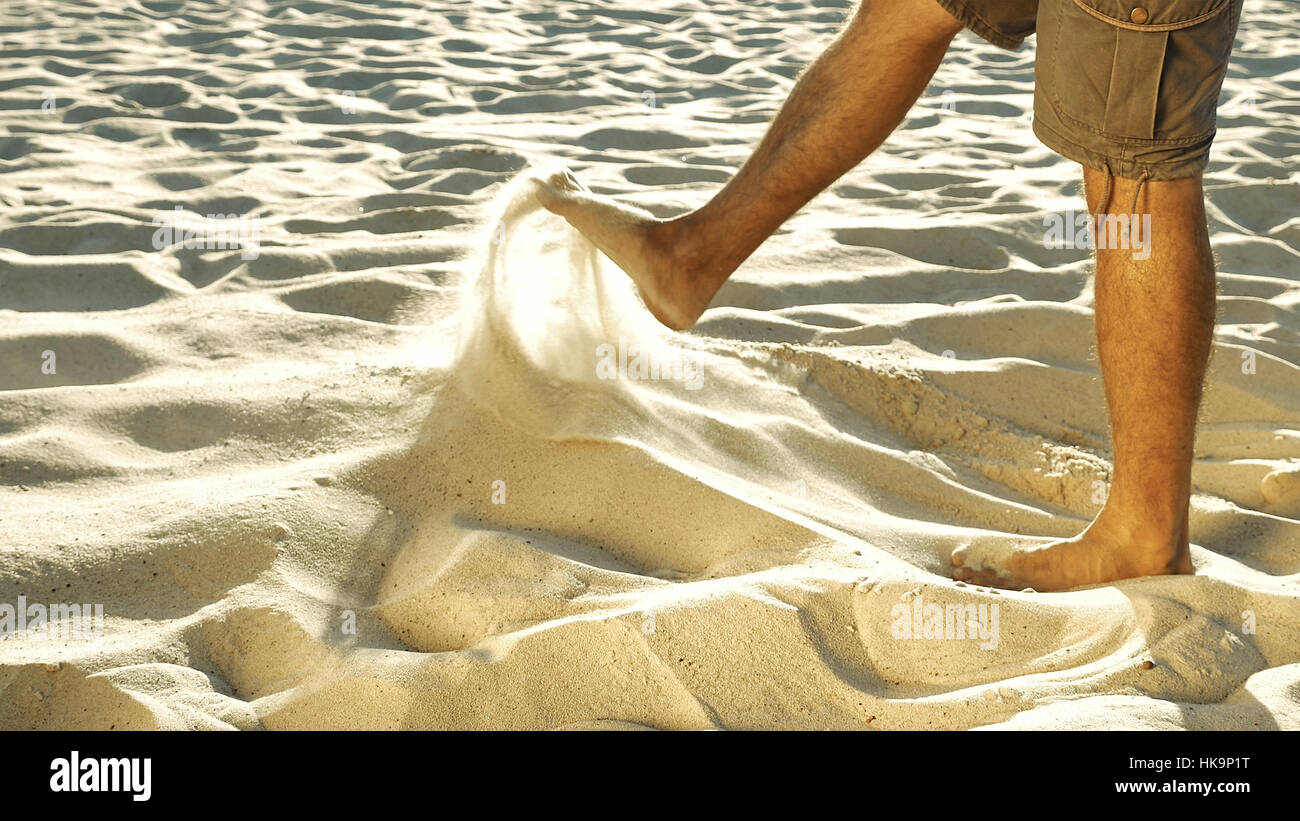 Man in khaki shorts sieving sand with feet Stock Photo
