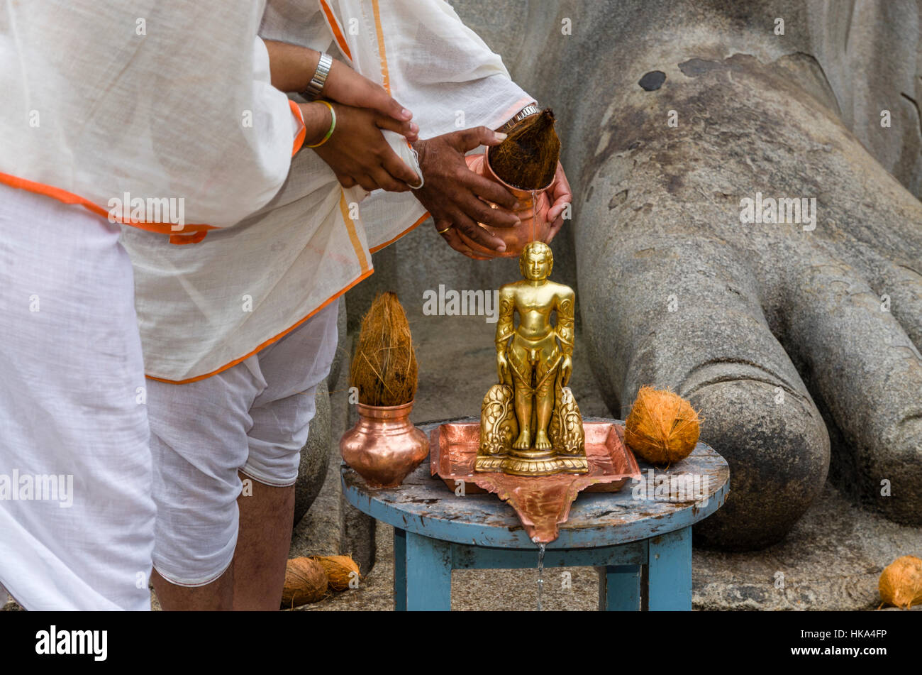 Two Jain pilgrims are pouring water on the small statue of Gomateshwara