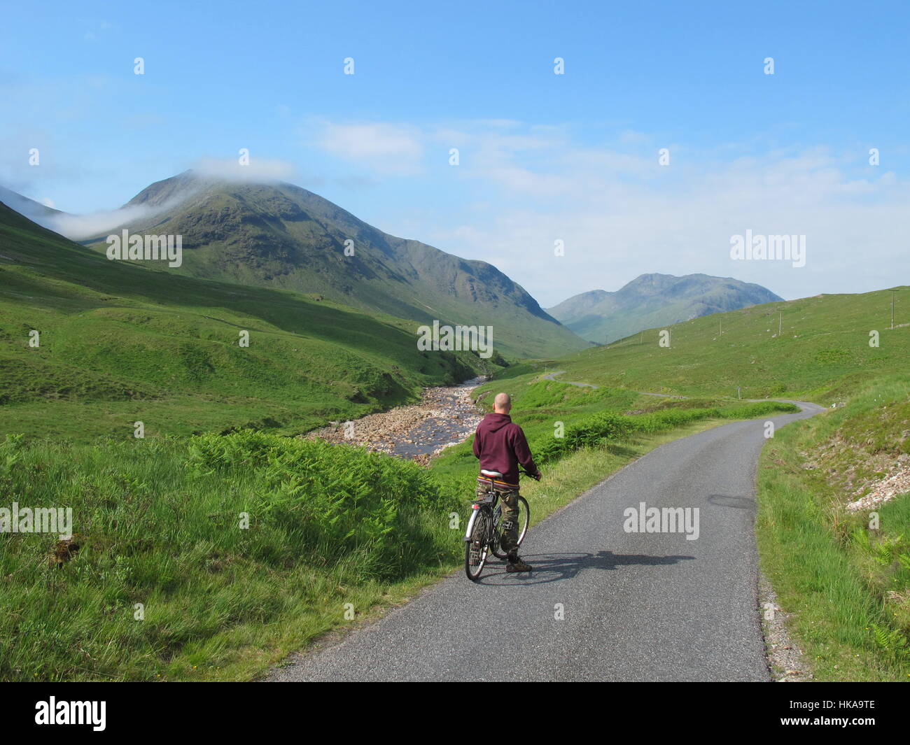 One cyclist cycling on a quiet country road towards Glen Etive in northwest highlands  Scotland UK Stock Photo