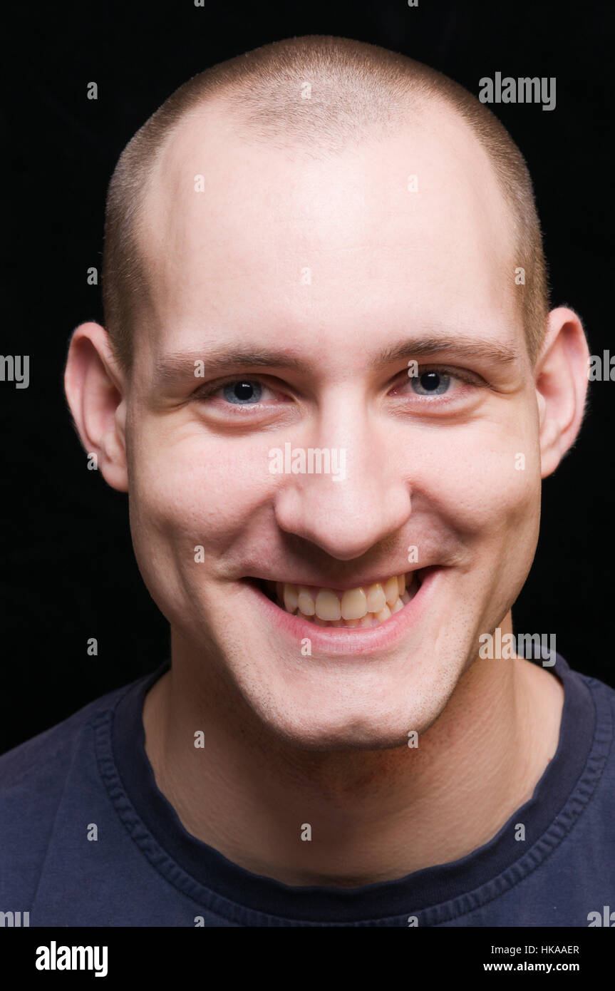 Frontal face portrait of a young man with his mouth open against a black background in the camera smiling Stock Photo