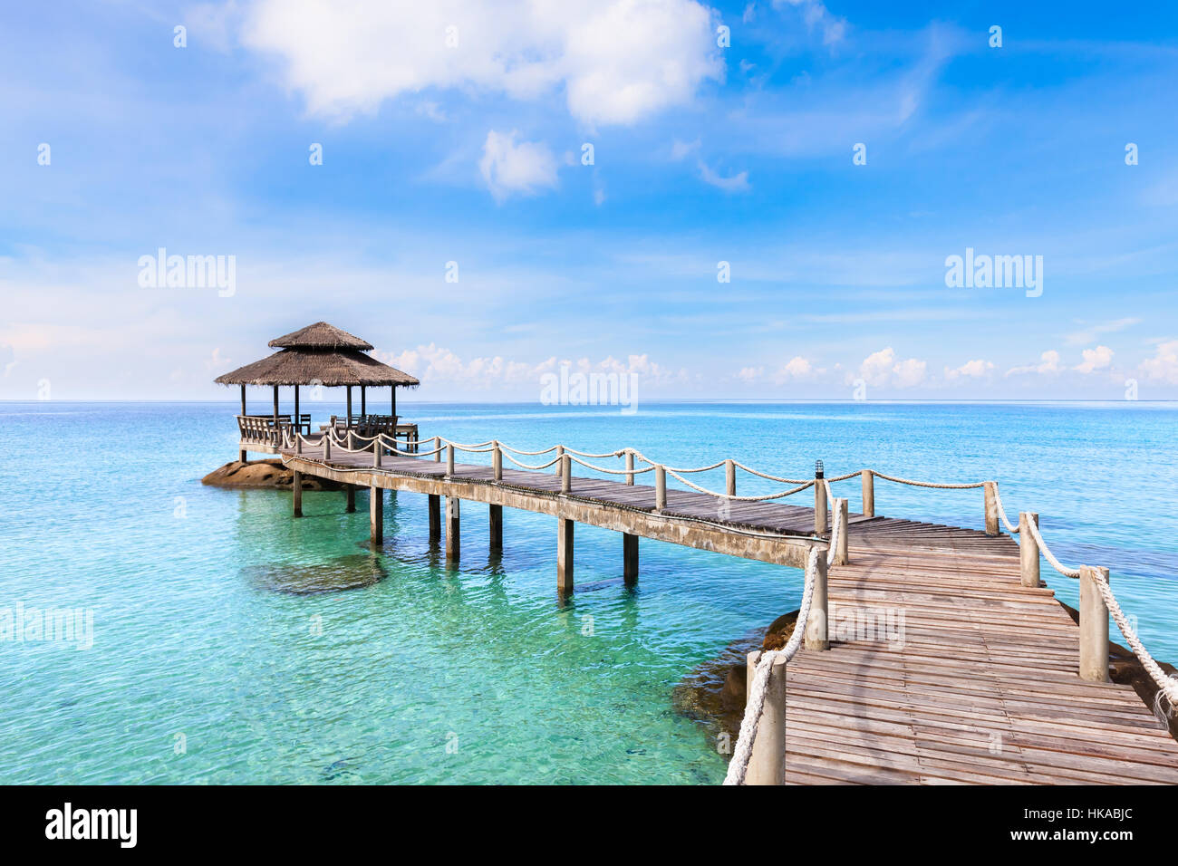 Tropical beach landscape with a wooden pier or jetty with hut above transparent turquoise clear sea water and blue sunny sky, beautiful vacation desti Stock Photo