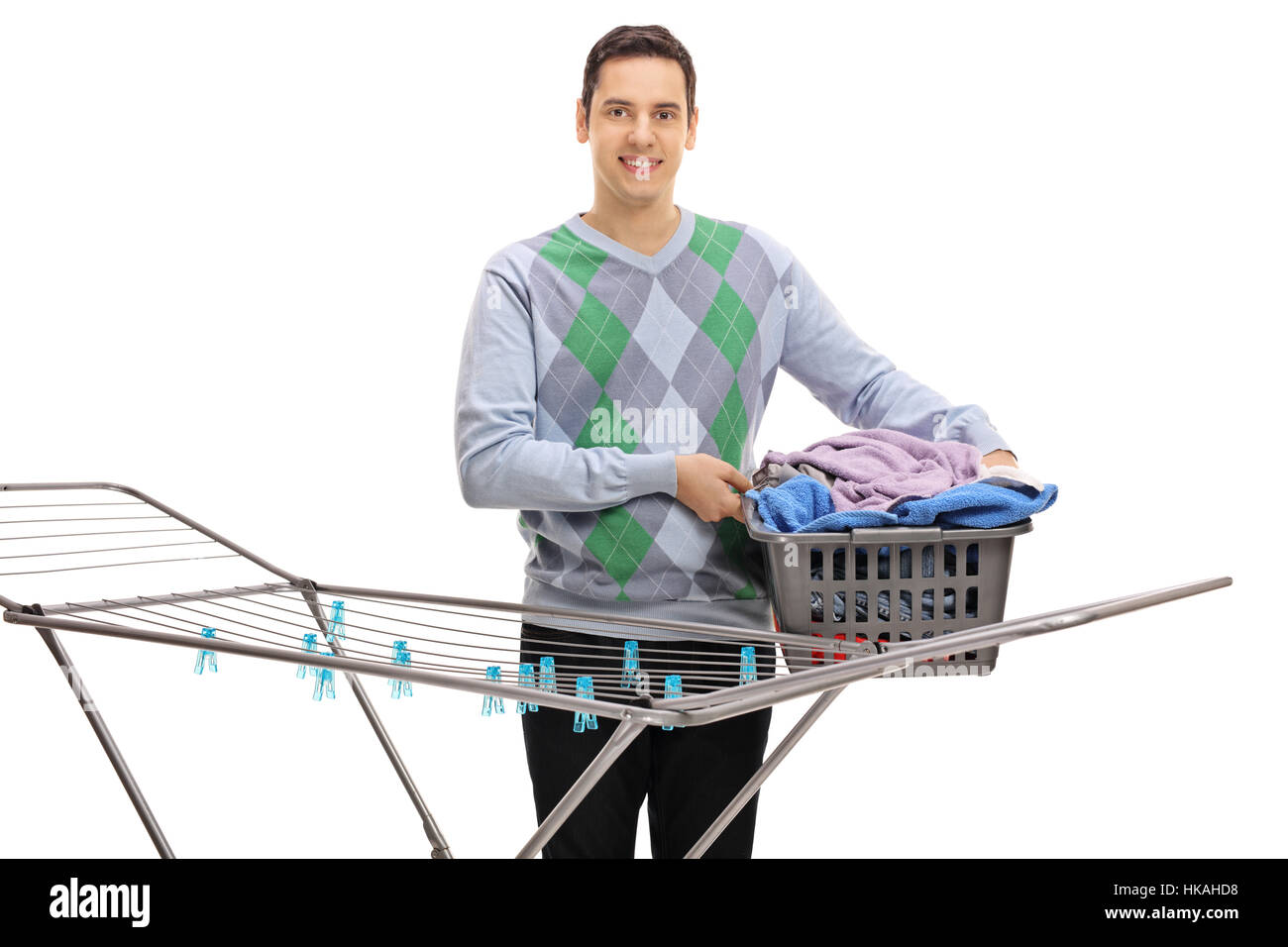 Young man holding a laundry basket full of clothes behind a clothing rack dryer isolated on white background Stock Photo