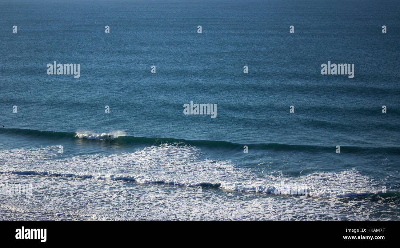 A surfer rides waves in an empty lineup at a beach called Chapel Porth, situated on the Cornish Coast. Stock Photo