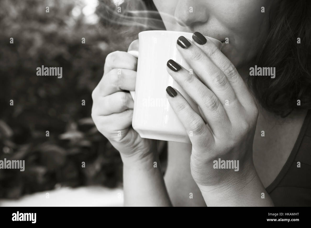 Young woman drinks coffee from white cup. Close-up black and white photo, selective focus on hands Stock Photo