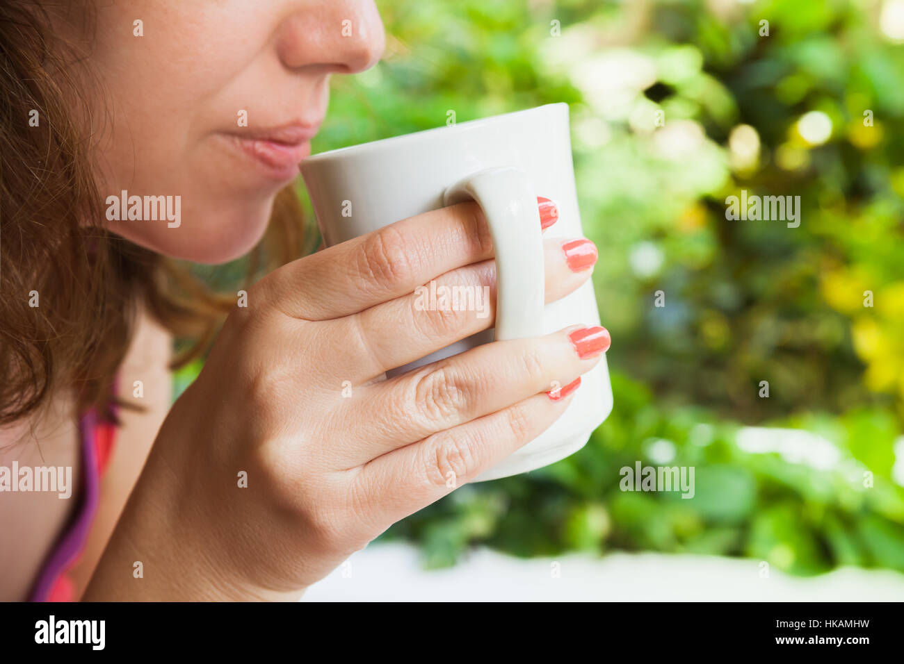 Young Caucasian woman drinks coffee from white cup. Close-up outdoor photo, selective focus on hand Stock Photo