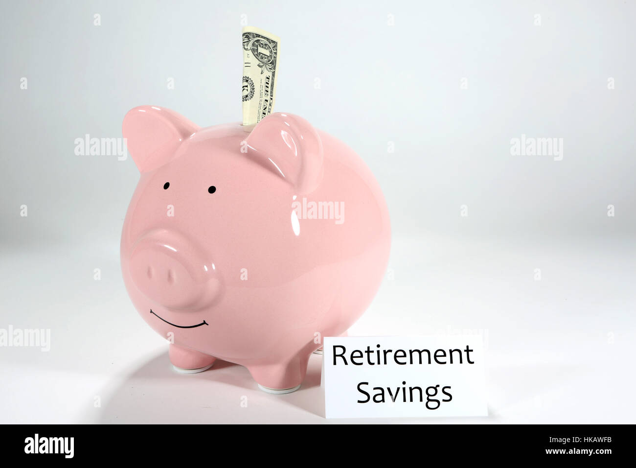 One dollar sticks partly in a pink piggy bank with a label stating retirement savings. Stock Photo