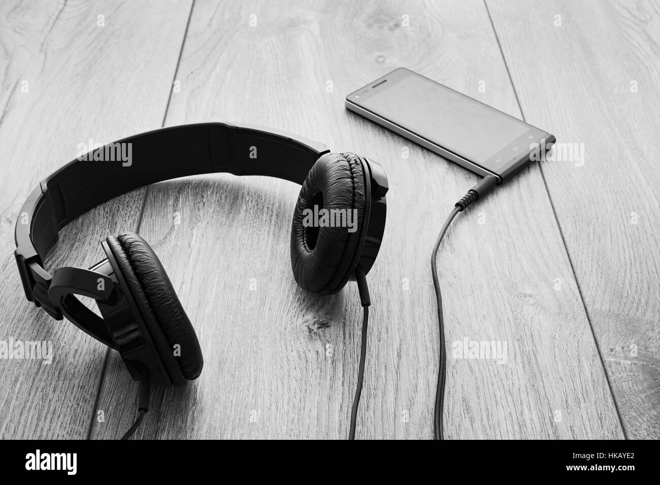 Black smartphone and black headphones on wood background. Selective focus on right earpiece of headphones. Black and white. Stock Photo