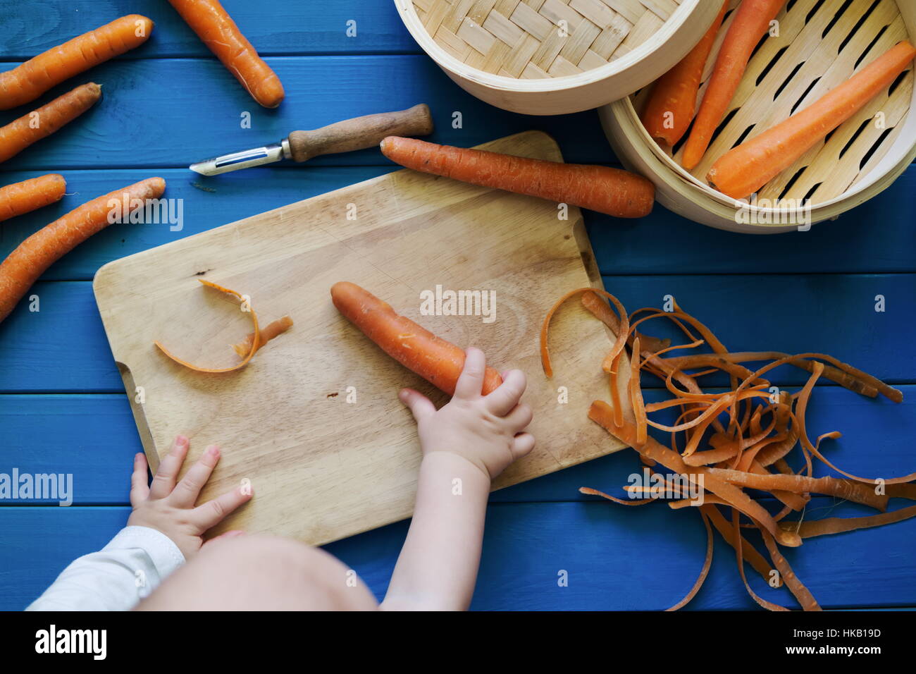 Small baby reaching for a carrot. Peeled and unpeeled carrots. Bamboo
