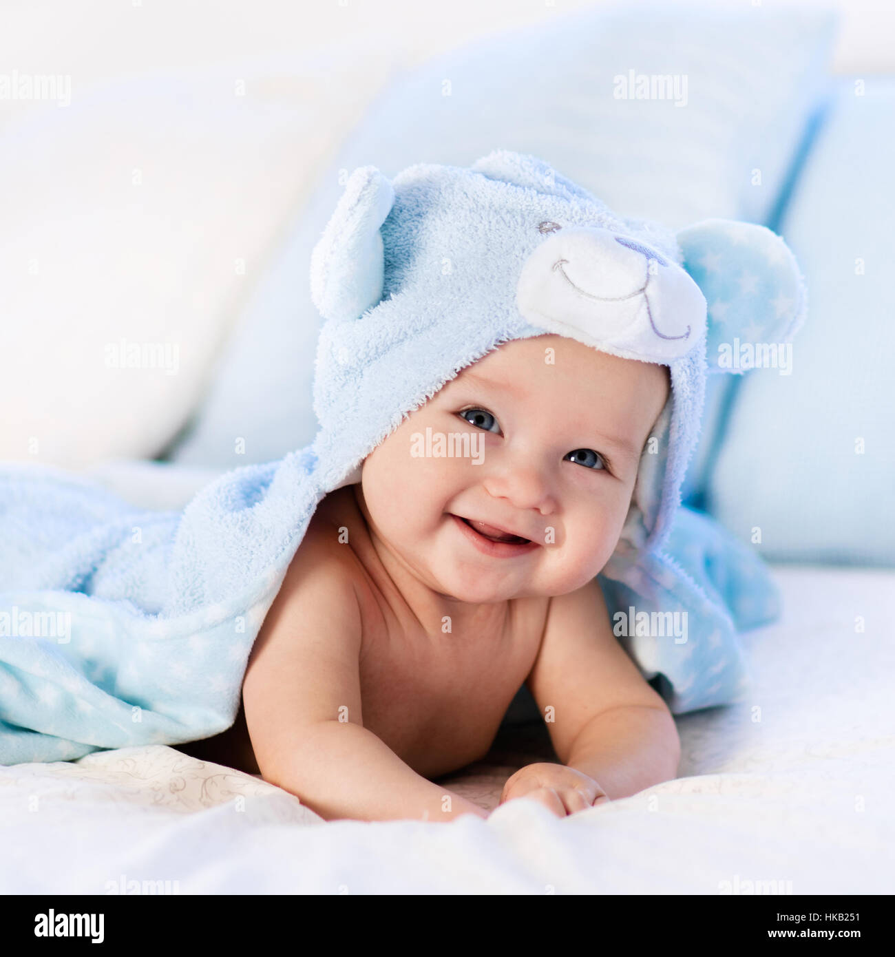 Baby boy wearing diaper and blue towel in white sunny bedroom. Newborn child relaxing in bed after bath or shower. Stock Photo