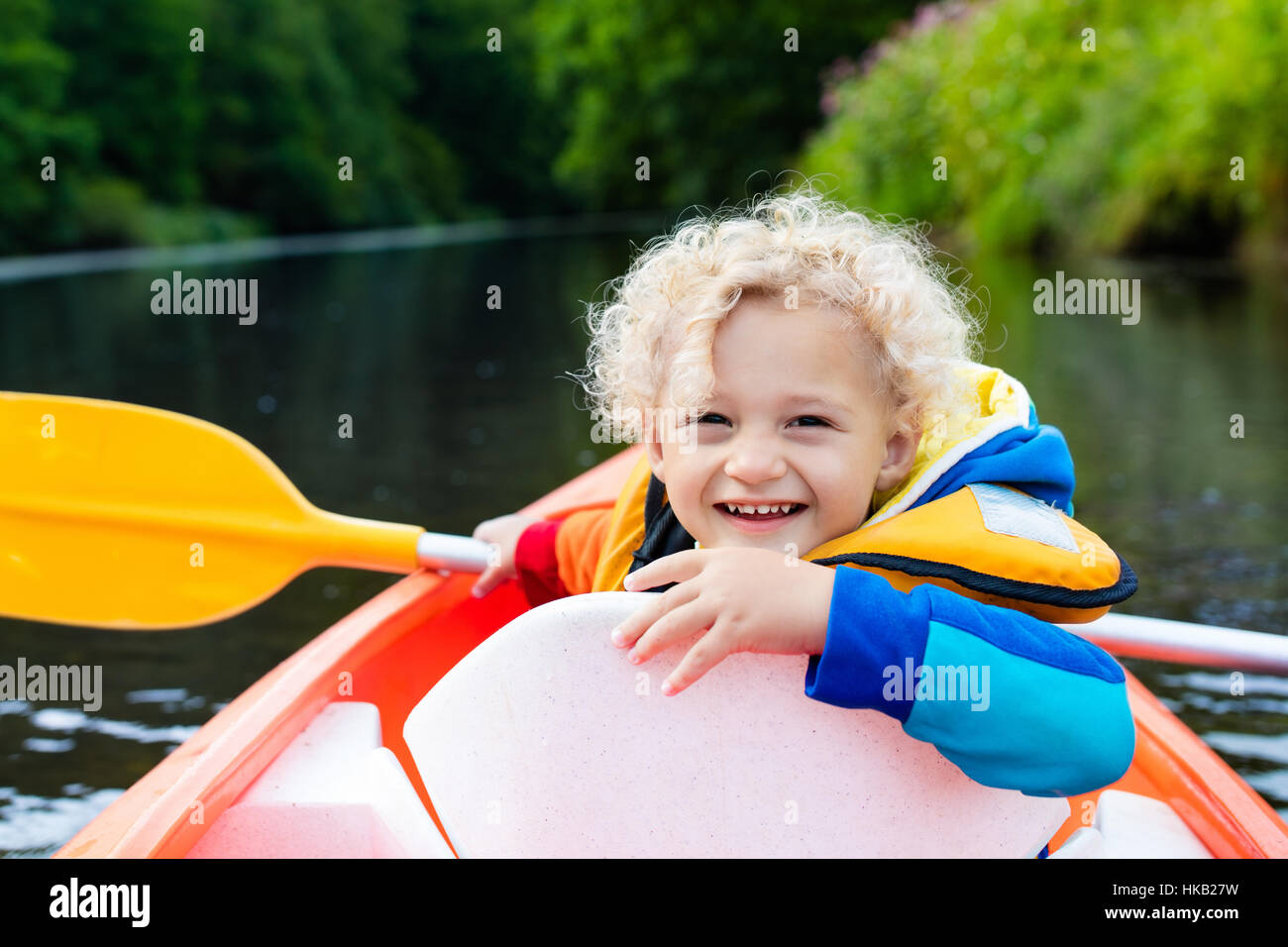Happy kid enjoying kayak ride on beautiful river. Little curly toddler ...