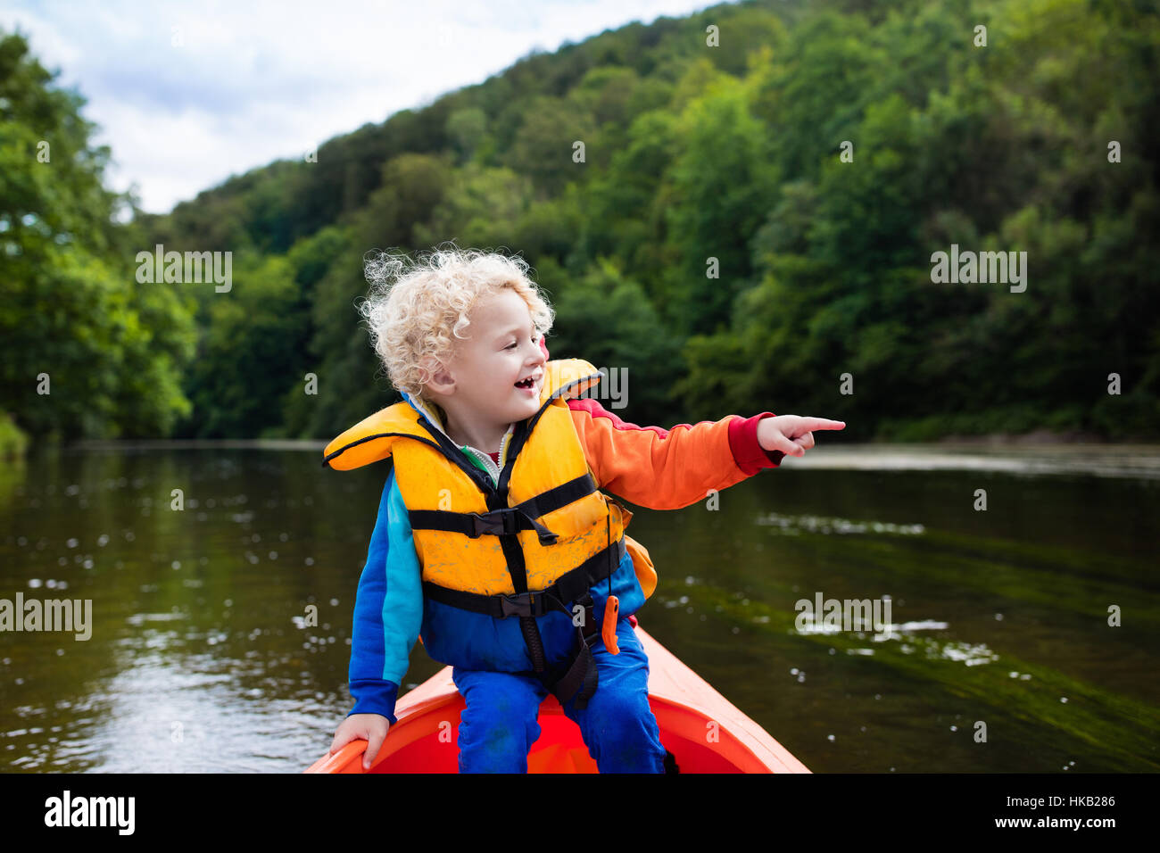 Happy kid enjoying kayak ride on beautiful river. Little curly toddler ...