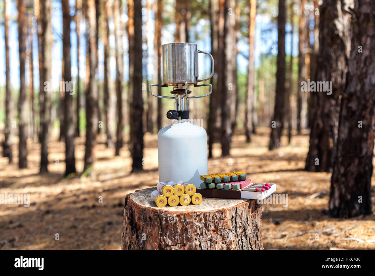 Gas burner in the forest. Gas burner with metal cup, cup of weapons ammunition and hunting matches on the stump in the forest. Stock Photo
