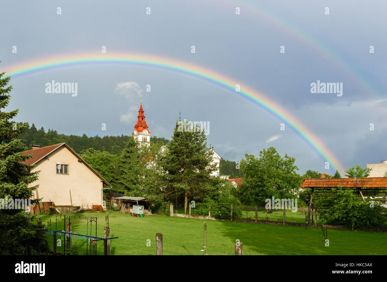 Double rainbow over a church in a cloudy village. Traditional farm with church in a village and double rainbow over woods and trees Stock Photo