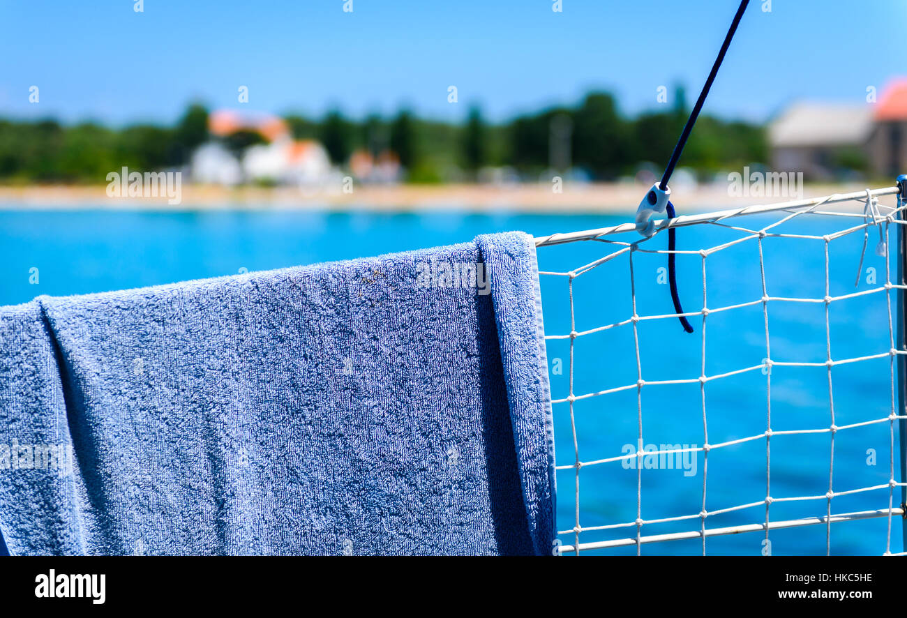 Blue Towel is hanging on a sailboat yacht fence. Drying a hand towel after a swim in blue sea on a vacation in Croatia. Stock Photo