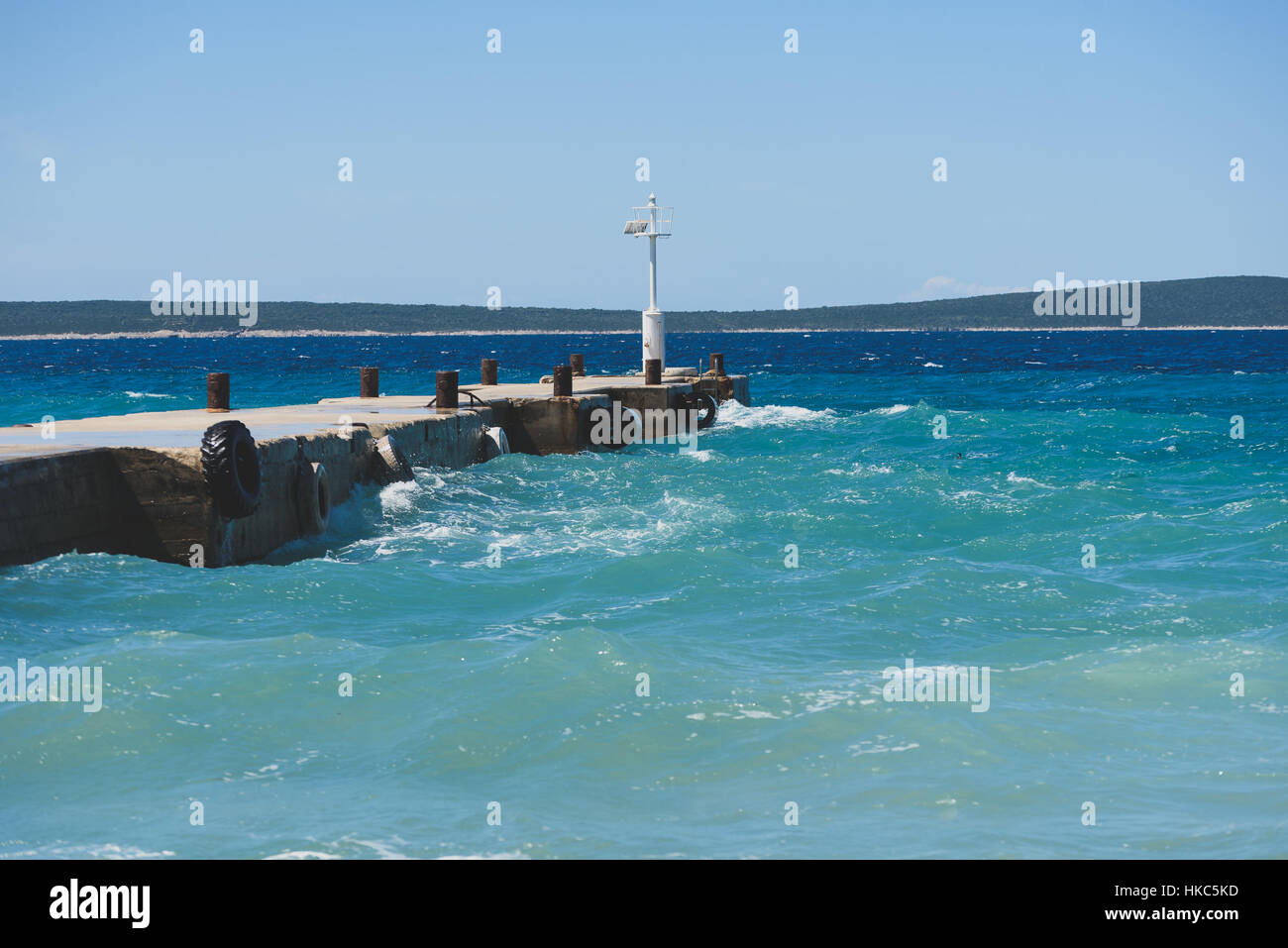 Strong winds and waves are hitting a pier in harbor. Port in Silba Croatia is experiencing bad windy weather. Stock Photo