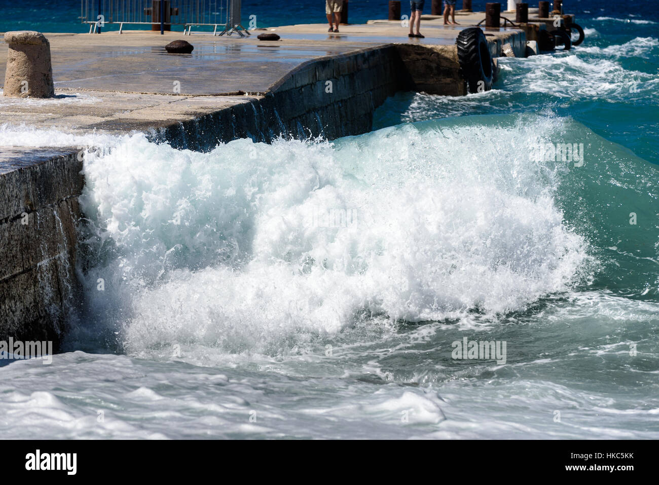 Strong winds and waves are hitting a pier in harbor. Port in Silba Croatia is experiencing bad windy weather. People are enjoying big waves. Stock Photo
