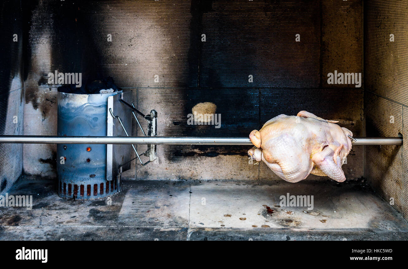 Cooking and preparing raw rotisserie chicken on the grill with Charcoal and Briquettes in the professional steak house or barbecue restaurant Stock Photo